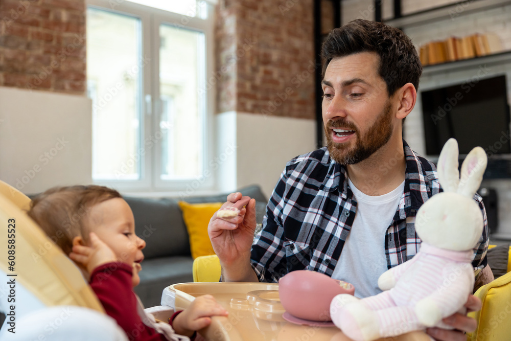 Father feeding his infant baby in home interior teaching toddler kid eating from spoon. Father feeding his infant baby in home interior teaching toddler kid eating from spoon.
