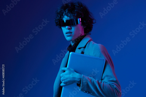 Portrait of a stylish male hacker with a laptop and futuristic glasses in blue light, Blue Perennial color, cyber security, technology, laptop copy space, template, trendy neon, freelance online work