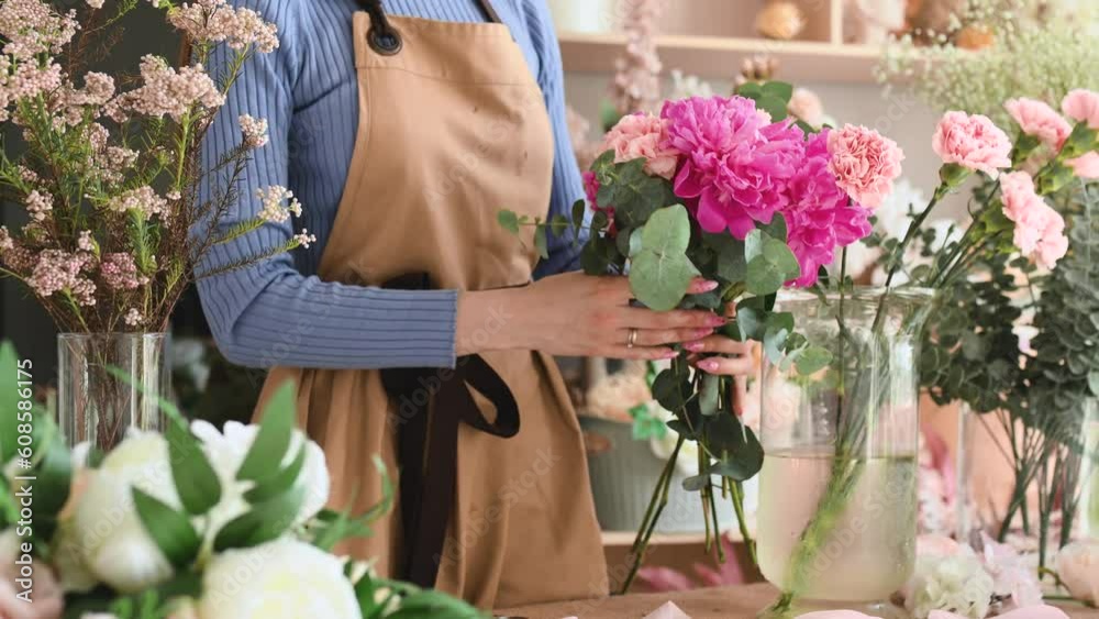 A woman florist makes a bouquet of peonies at her decorations studio. Floral design studio, making decorations and arrangements. Flower delivery, order creation. Closeup no face