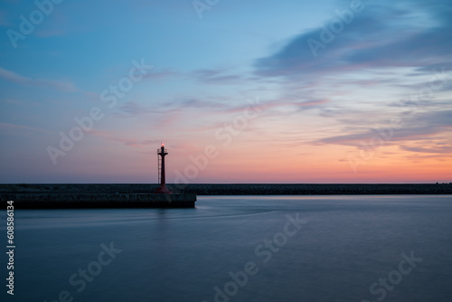 The lighthouse at harbor with clouds in golden hour.The quite beautiful orange tone sunset at Tainan quigu of Taiwan.The sky had fantastic hue and the sea looks quite peaceful.It's long exposure photo