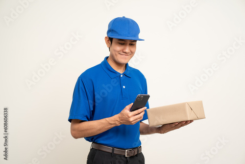 Asian man in blue uniform standing holding box parcel cardboard and smartphone on isolated white background. Male service worker with cell phone. Delivery courier shipping service