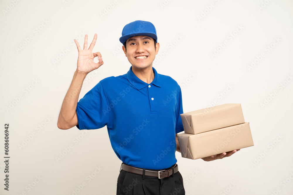 Asian man in blue uniform standing holding box parcel cardboard and smartphone on isolated white background. Male service worker with cell phone. Delivery courier shipping service Asian man in blue uniform standing holding box parcel cardboard and smartphone on isolated white background. Male service worker with cell phone. Delivery courier shipping service