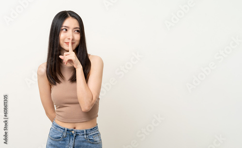 Happy beautiful asian woman whispering some secret gossip. Excited pretty girl index finger on mouth standing pose on isolated white background. © Chanakon