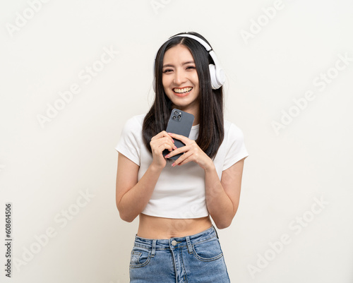 Beautiful young asian women choose song and play music from smartphone connection with wireless headphone having fun. Teenage girl listen to the music enjoy relaxing on isolated white background. © Chanakon