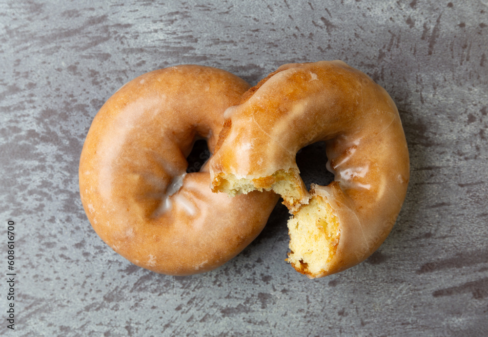 Top view of a bitten and whole freshly baked cake donut on a gray mottled countertop.