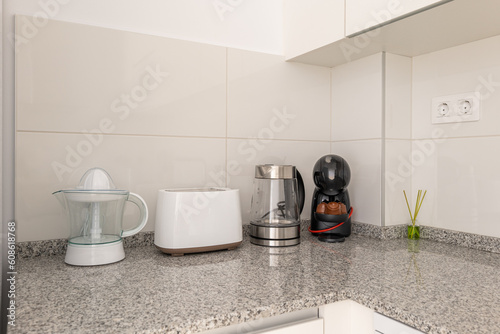 Close-up of a kitchen table with a juicer and kitchen appliances with white tiles and kitchen cabinets. The concept of household utensils and convenient gadgets for cooking