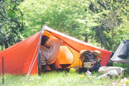 ソロキャンプをしている若い日本人女性/朝起きてテントの外に出ようとしている 