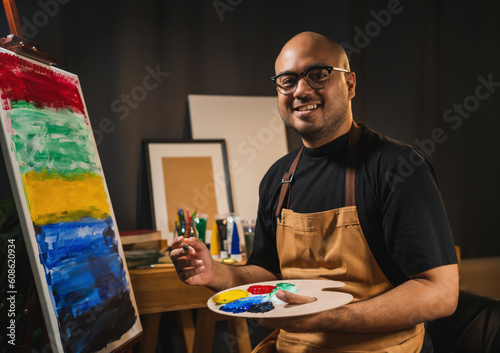 Asian man in the darkroom warm light artist working on painting with brush and variant acrylic color. Man artist painter on canvas in creative studio as art concept