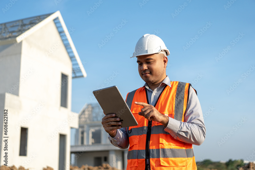 Confident asian engineer man Using tablet for checking and maintenance to inspection at modern home building construction. Architect working with white safety helmet in construction site