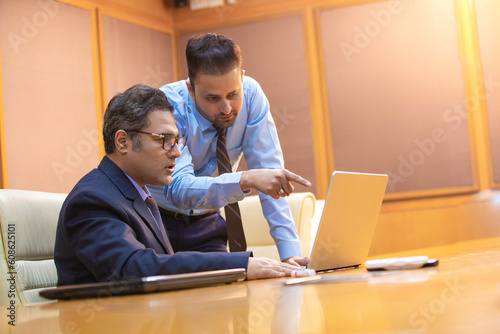 Young Indian manager showing project detail in laptop and discussing with his boss or senior.
