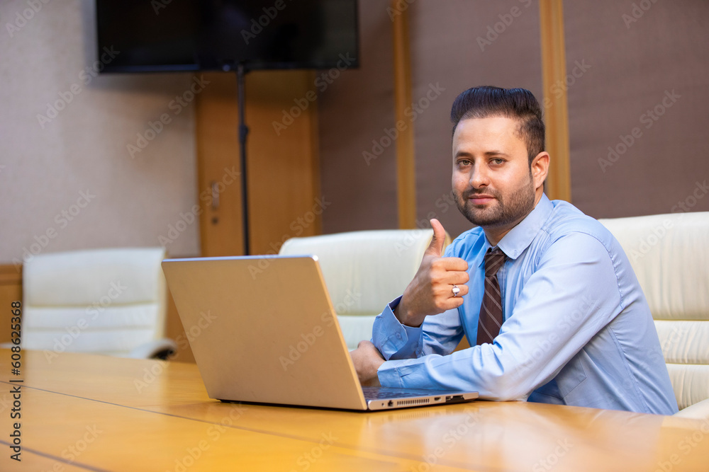 Indian corporate man using laptop and showing thumps up at office. Indian corporate man using laptop and showing thumps up at office.