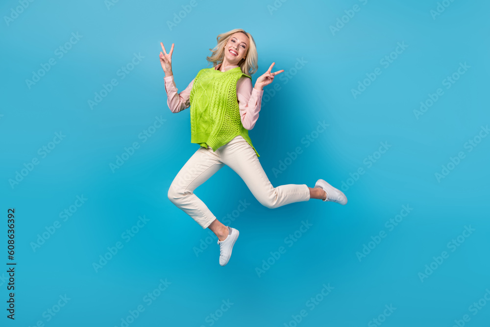 Full body photo of pretty overjoyed lady jumping demonstrate v-sign isolated on blue color background