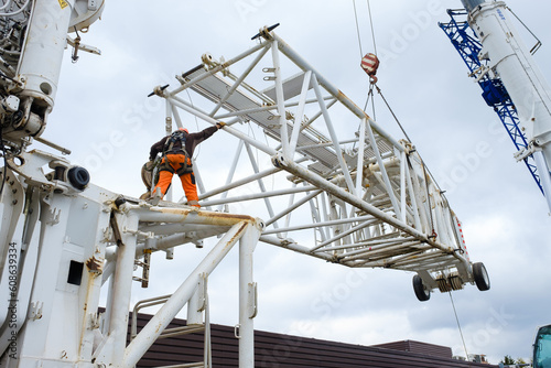 worker in hard hat and hi-vis guides jib extension for 1000 ton mobile crane into position