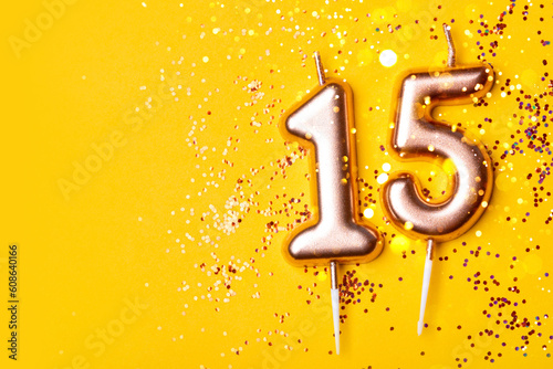 Gold candles in the form of number fifteen on yellow background with confetti. 15 years celebration.