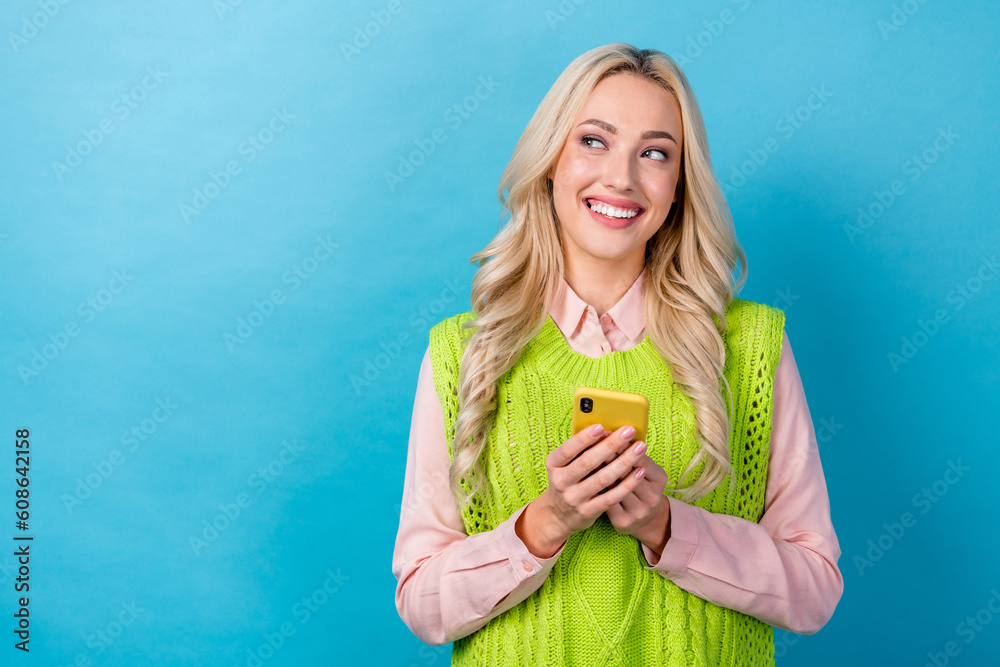 Photo of pretty cheerful girl toothy smile hold smart phone look empty space isolated on blue color background Photo of pretty cheerful girl toothy smile hold smart phone look empty space isolated on blue color background