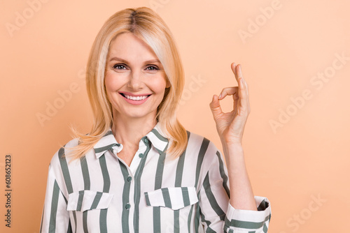 Photo of cheerful confident lady wear striped shirt smiling showing okey gesture isolated beige color background