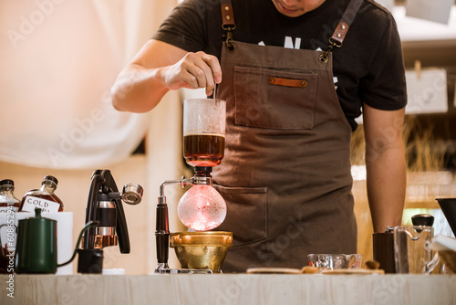 Professional coffee maker - Barista using coffee siphon brewing hot espresso at coffee shop coffee brewing syphon alternative method. Startup Business Concept.