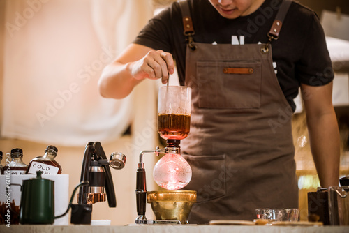 Professional coffee maker - Barista using coffee siphon brewing hot espresso at coffee shop coffee brewing syphon alternative method. Startup Business Concept.