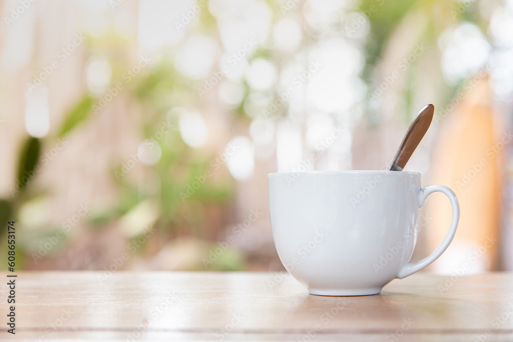 A morning cup of coffee on a wooden table with blurry bokeh from the trees in the background. A morning cup of coffee on a wooden table with blurry bokeh from the trees in the background.