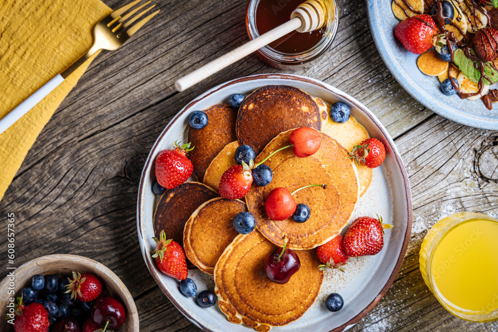 American pancakes with blueberries, strawberries and cherries with dip of honey. Placed on a rustic designer plate, on wooden rustic board. American pancakes with blueberries, strawberries and cherries with dip of honey. Placed on a rustic designer plate, on wooden rustic board.