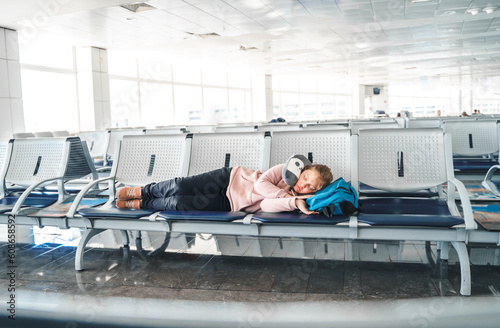 Kid, teen tired girl sleeping, waiting in airport passenger terminal departure hall with backpack. Sitting on chairs in airplane travel pillow. Flight delay.Family summer vacation,travel holiday tour