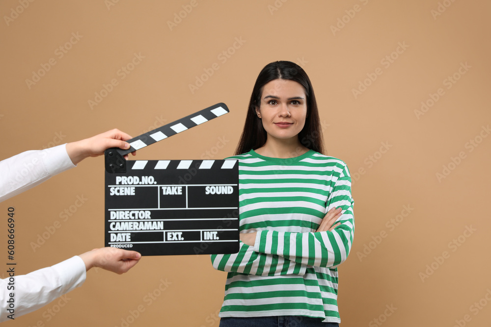 Actress performing while second assistant camera holding clapperboard on beige background. Film industry