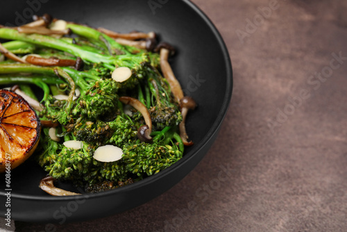 Tasty cooked broccolini with lemon and mushrooms on grey table, closeup. Space for text photo