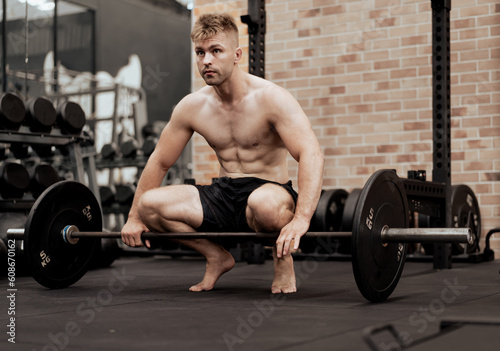 Muscular naked chest man doing deadlift exercise in fitness gym. Young healthy bodybuilder athlete lifting barbell to strength body muscles. Heavy weightlifting is best for biceps workout exercise.