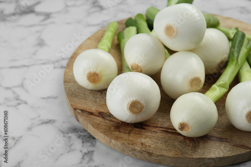 Wooden board with green spring onions on white marble table  closeup. Space for text