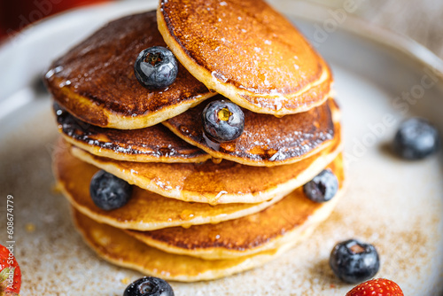 American pancakes with blueberries, strawberries and cherries with dip of honey. Placed on a rustic designer plate, on wooden rustic board. 