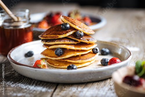 American pancakes with blueberries, strawberries and cherries with dip of honey. Placed on a rustic designer plate, on wooden rustic board. 
