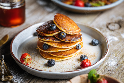 American pancakes with blueberries, strawberries and cherries with dip of honey. Placed on a rustic designer plate, on wooden rustic board. 