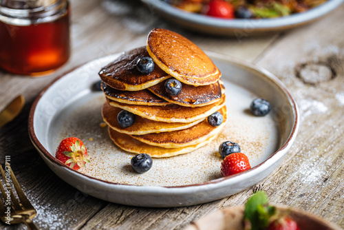American pancakes with blueberries, strawberries and cherries with dip of honey. Placed on a rustic designer plate, on wooden rustic board. 