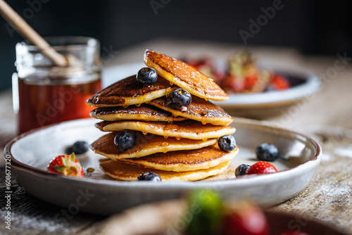 American pancakes with blueberries, strawberries and cherries with dip of honey. Placed on a rustic designer plate, on wooden rustic board. 
