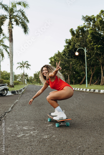 Happy asian girl is riding a skateboard on an empty sunny road, laughing and smiling. Freedom and happiness.