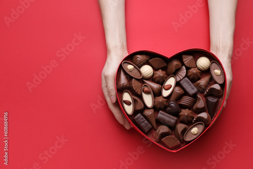 Woman holding heart shaped box with delicious chocolate candies on red background, top view. Space for text © New Africa