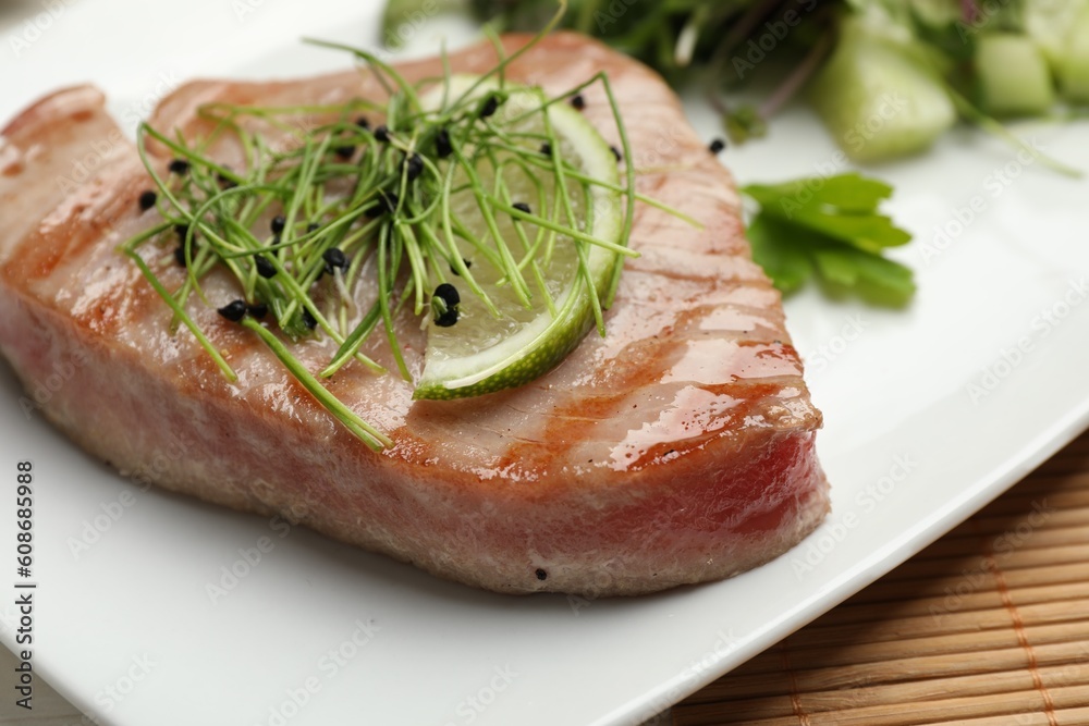 Delicious tuna steak with microgreens and lime on plate, closeup