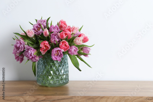 Beautiful bouquet of colorful tulip flowers on wooden table near white wall. Space for text