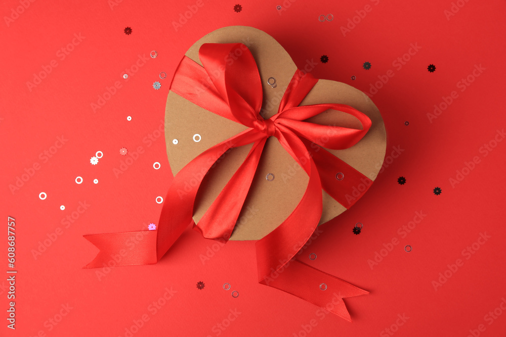Beautiful heart shaped gift box with bow and confetti on red background, top view Beautiful heart shaped gift box with bow and confetti on red background, top view