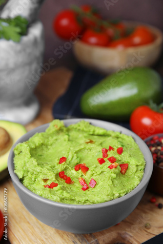 Bowl of delicious guacamole and ingredients on wooden board, closeup
