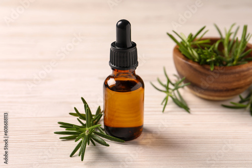 Bottle with essential oil and fresh rosemary on white wooden table