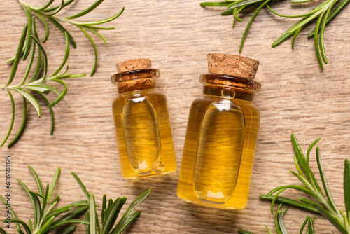 Bottles with essential oil and fresh rosemary on wooden table, flat lay