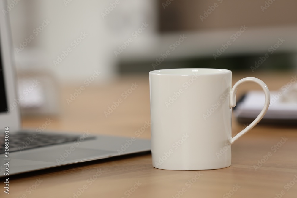 White ceramic mug and laptop on wooden table at workplace. Space for text White ceramic mug and laptop on wooden table at workplace. Space for text
