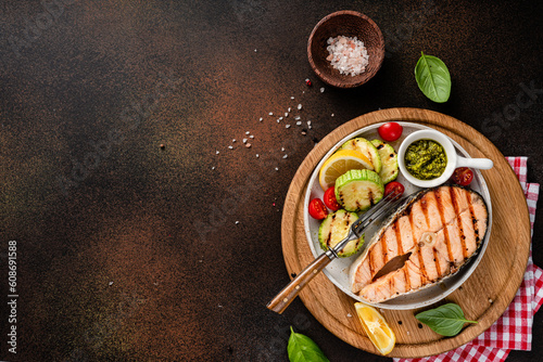 Grilled salmon steaks with spices, lemons and grilled zucchini on wooden board. Top view of fried fish with copy space. Keto recipe.