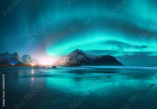 Northern Lights and beach at starry night in winter. Lofoten islands  Norway. Beautiful Aurora borealis. Sky with polar lights. Landscape with aurora  sea with sky reflection in water  mountains
