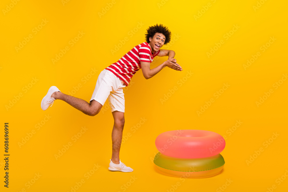 Full length photo of excited cool guy wear striped t-shirt diving inside two inflatable rings isolated yellow color background