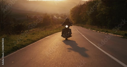A man driving a motorbike through an empty highway during beautiful sundown.