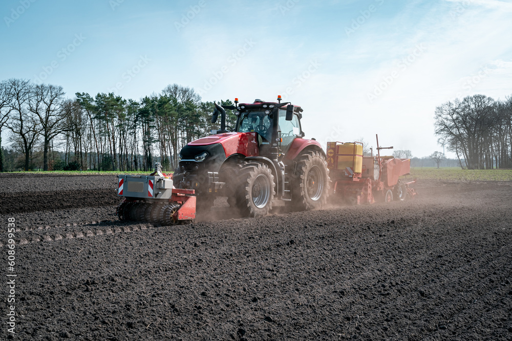 Fototapeta premium Staubige Angelegenheit - Trecker mit moderner Kartoffellegemaschine beim Kartoffel legen, im Staub.