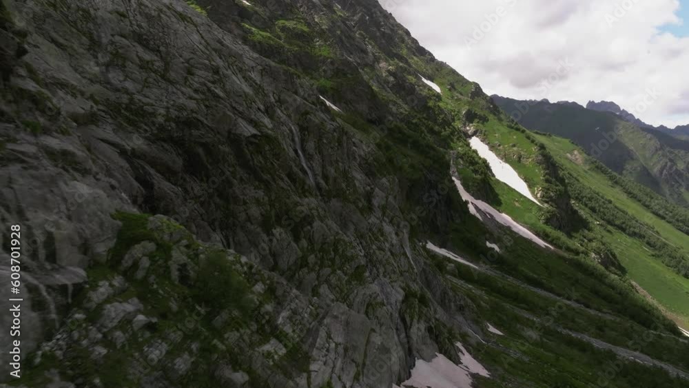 Picturesque canyon or valley with waterfalls. Snow-covered mountains covered with lush green grass and trees on a summer sunny day with clouds Picturesque canyon or valley with waterfalls. Snow-covered mountains covered with lush green grass and trees on a summer sunny day with clouds