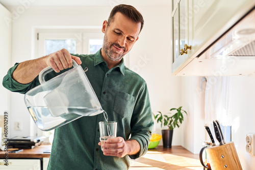 Man pouring water from a filter jug into a glass in the kitchen